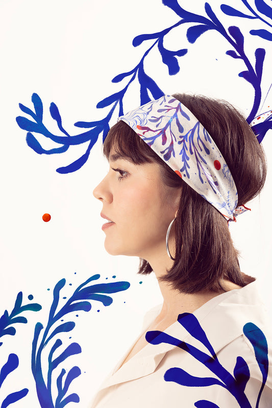 Side profile of a woman using a patterned silk scarf as a headband.
