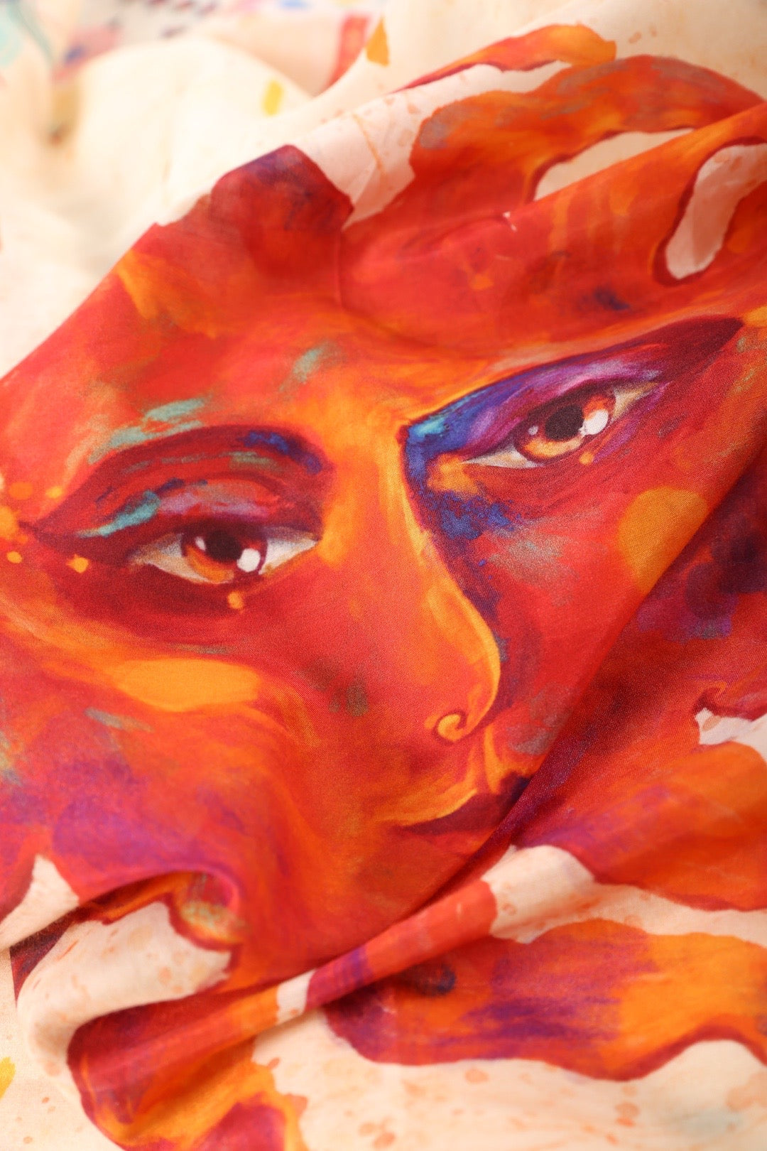 Detailed macro shot of the hand-painted sun face illustration on a Journey of Yula silk twill scarf.