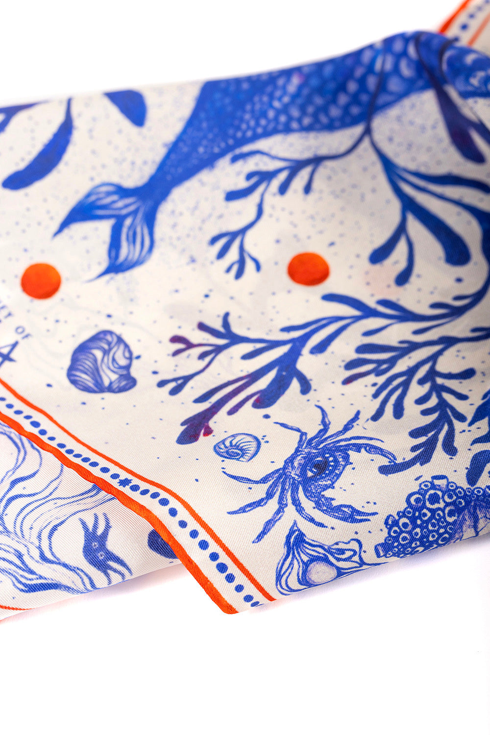 Close-up detail of silk scarf with blue and orange marine life illustrations.