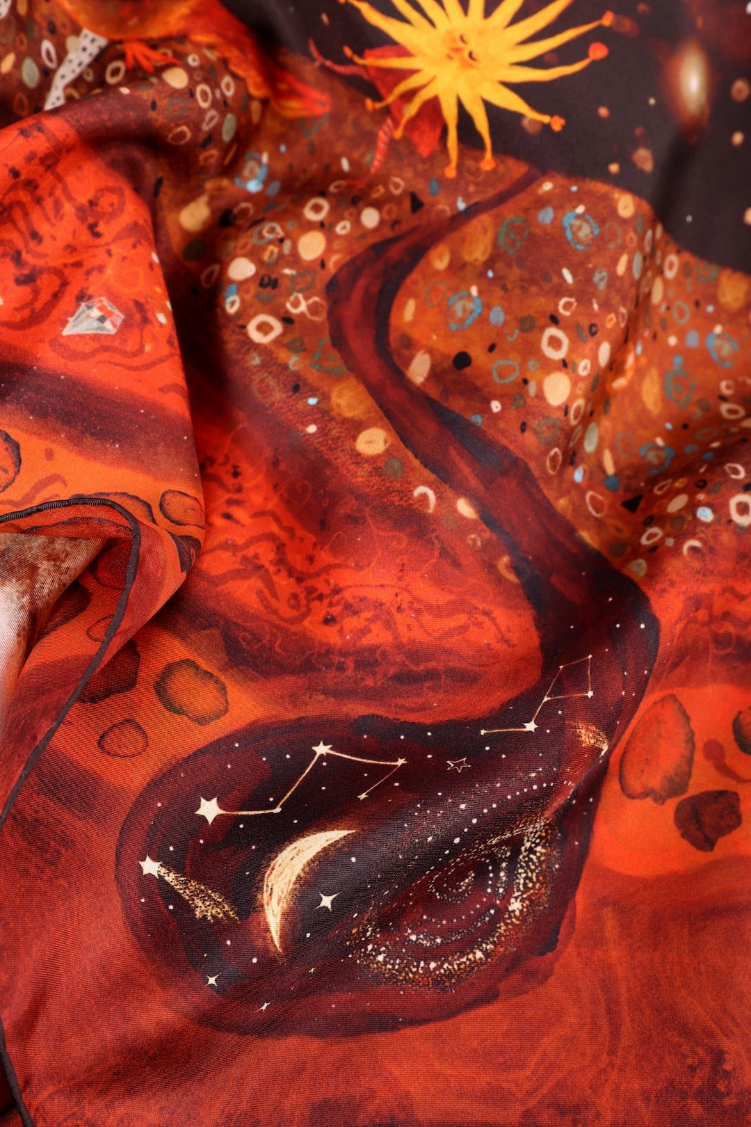 Macro shot of vibrant orange and red cosmic art on a premium silk scarf fabric.