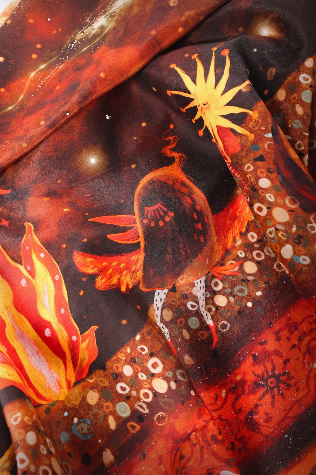Detailed view of whimsical sun, fire, and cosmic bird illustrations from the Journey of Yula scarf collection with intricate textures.