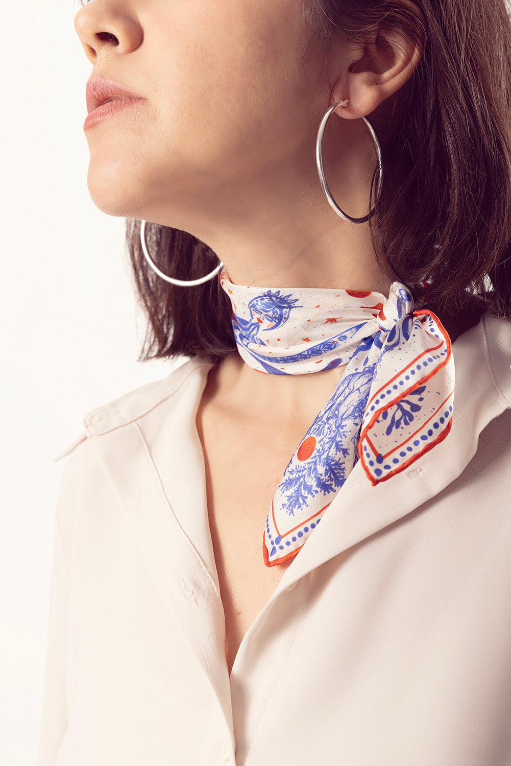 Close-up of a blue and orange detailed silk scarf knotted over a white shirt.