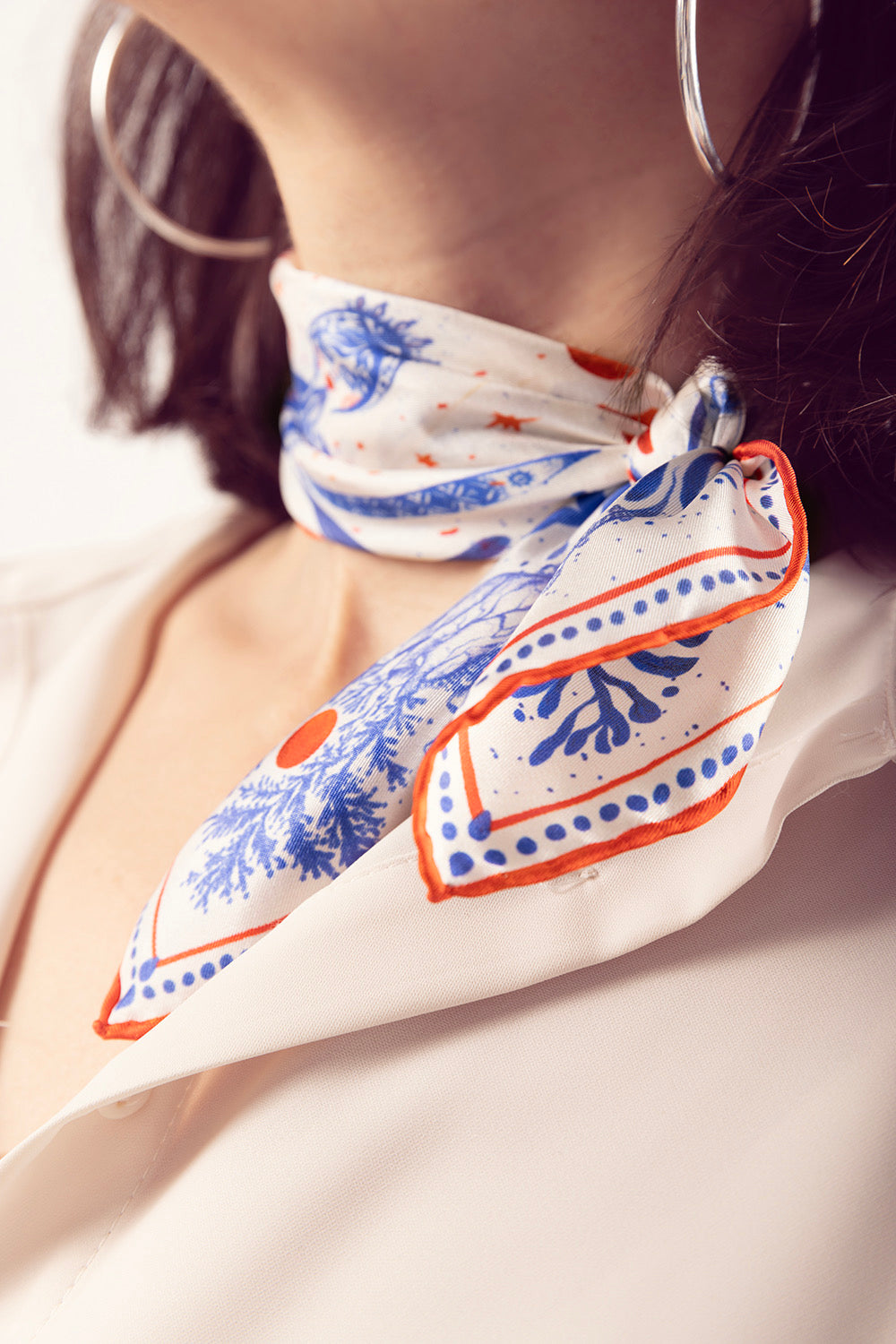 Close-up of a blue and orange detailed silk scarf knotted over a white shirt.