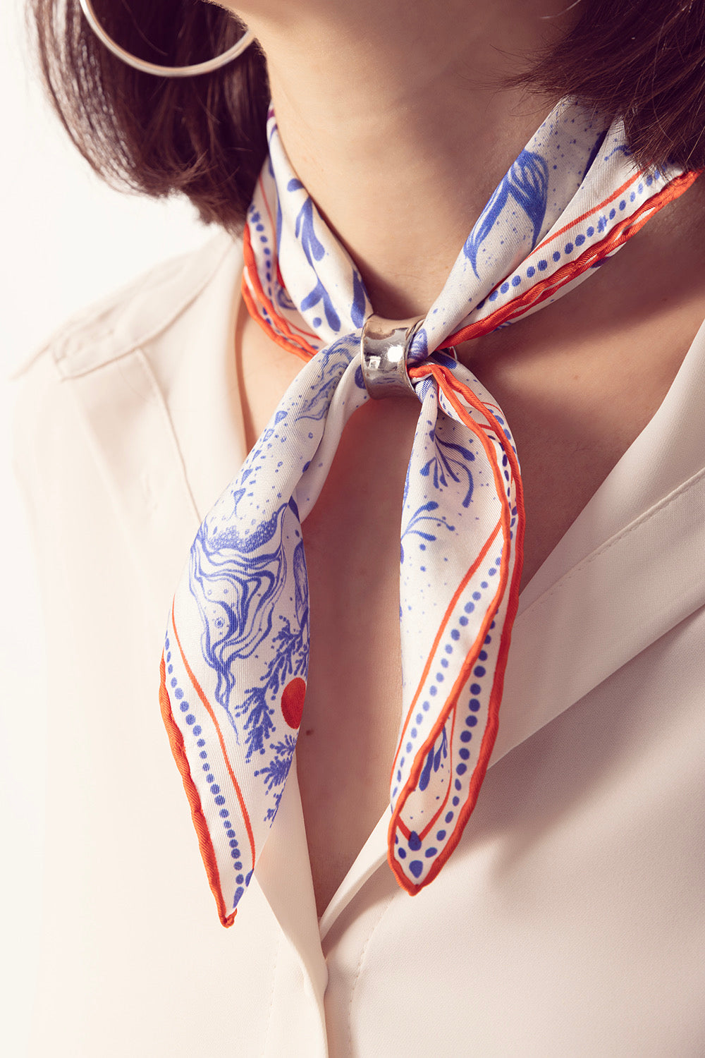 Silk scarf styled with a silver scarf ring accessory on a white shirt.