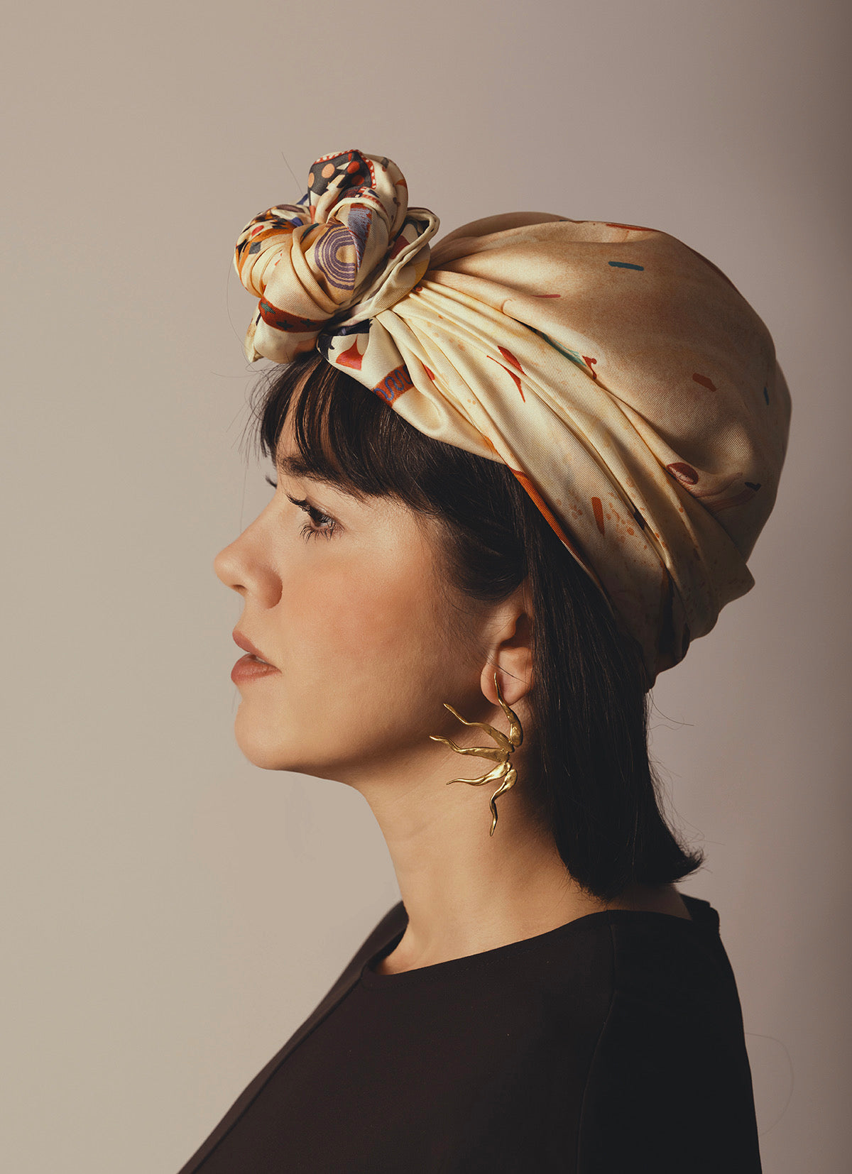 Profile view of a woman wearing a premium silk scarf tied as a stylish turban, paired with gold statement earrings.