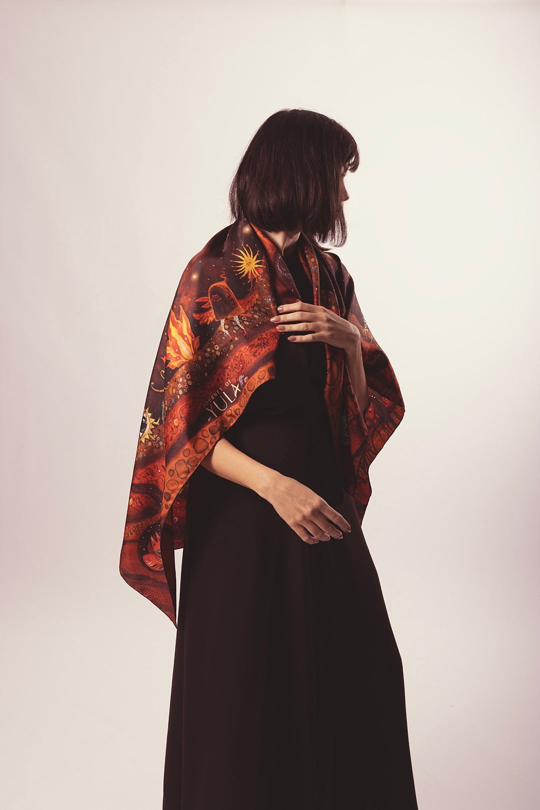 Elegant woman wearing a designer silk scarf with a cosmic theme over a black dress.