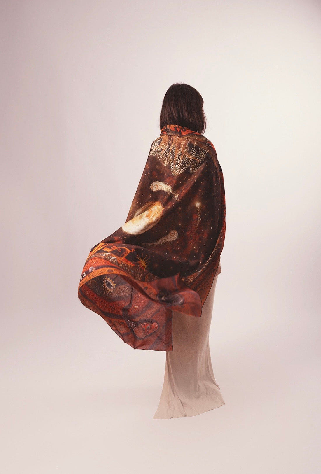Back view of a model elegantly draping an illustrated celestial scarf featuring deep space and earthly root patterns like a cape.