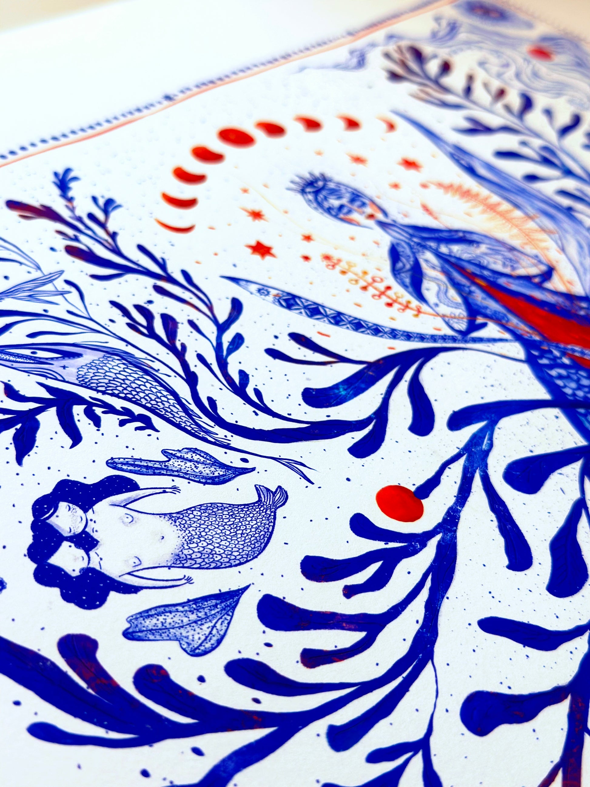 Close-up detail of a blue and orange ink illustration featuring moon phases, a mermaid figure, and intricate coral patterns.