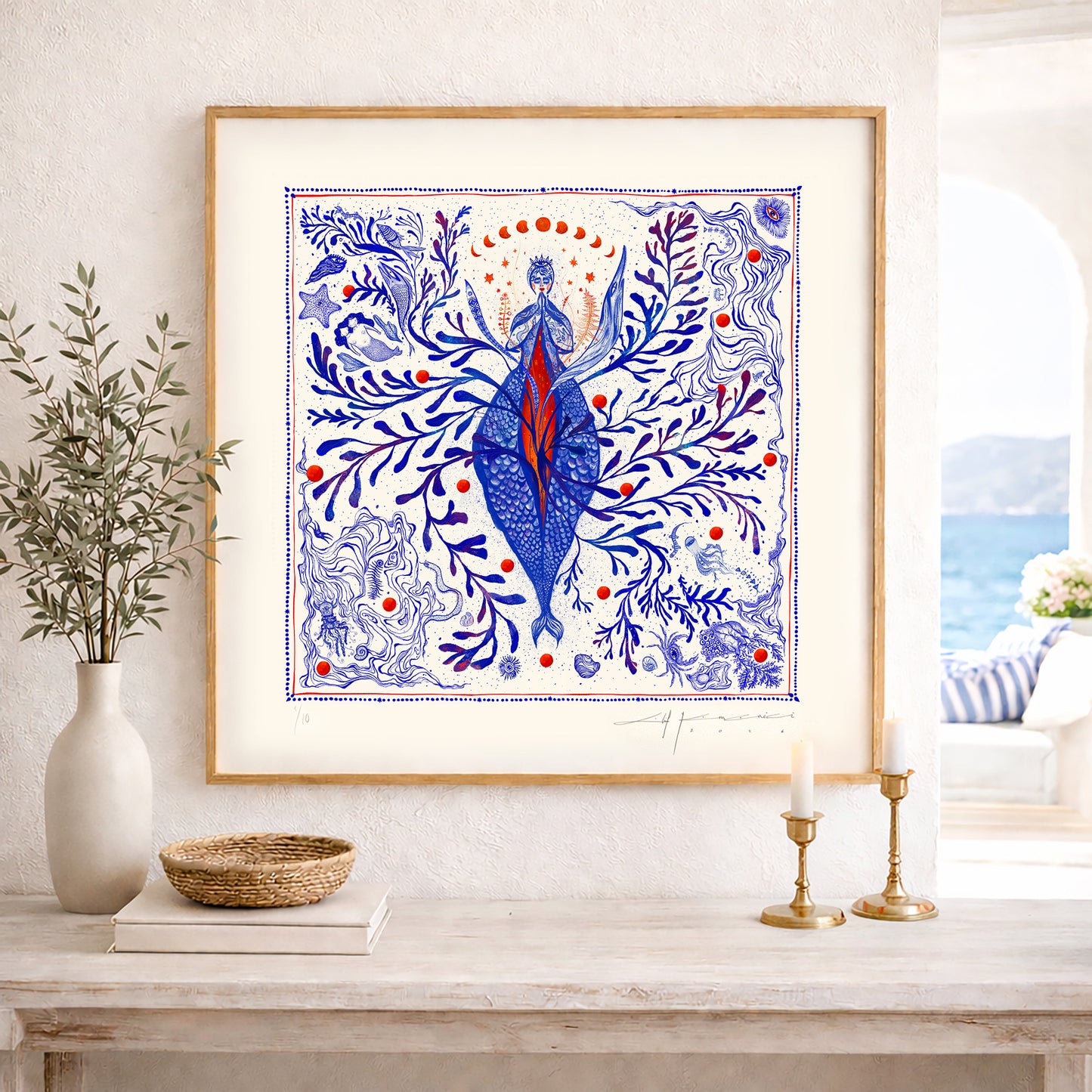 A framed square nautical illustration displayed on a wooden console table in a bright, modern interior setting by the sea.