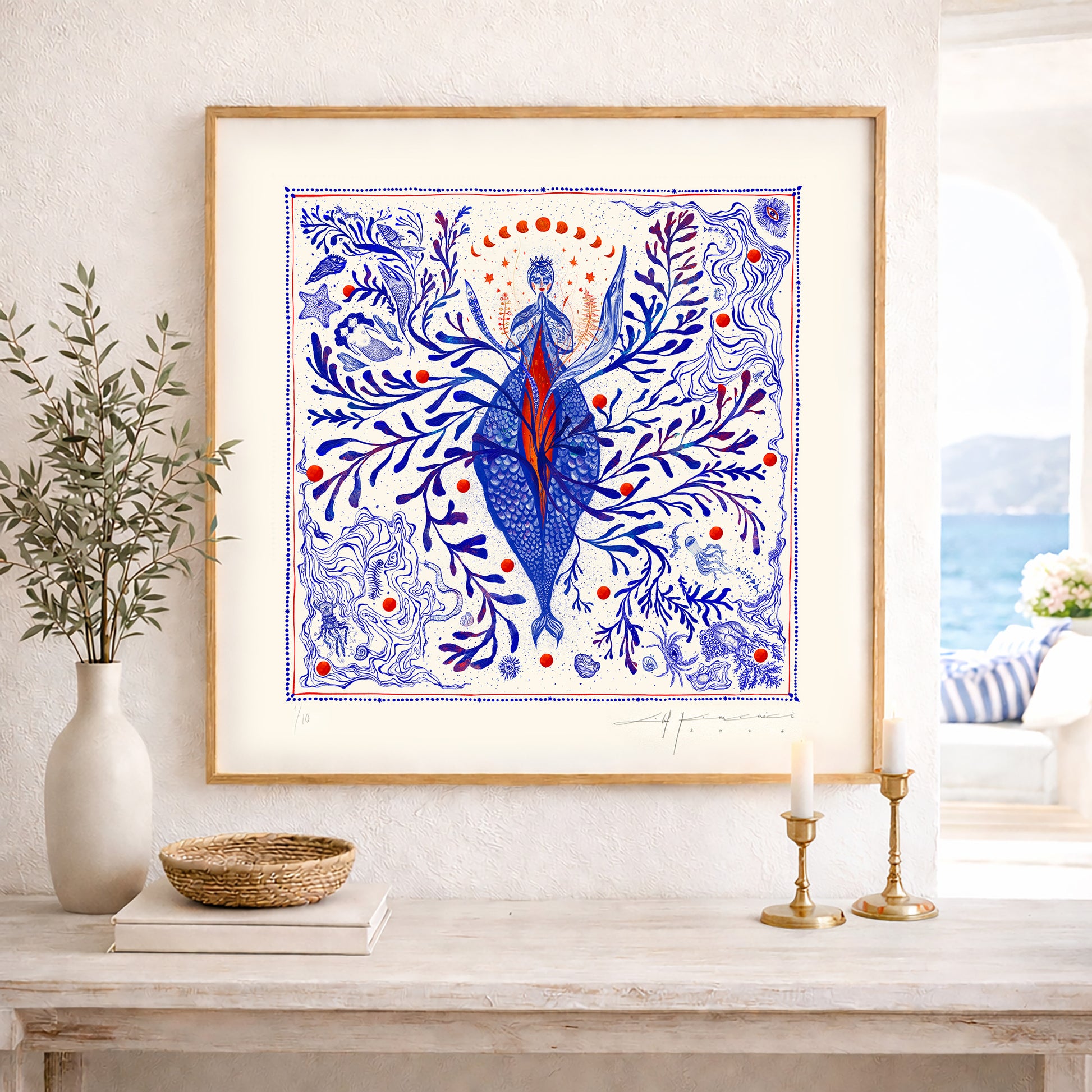 A framed square nautical illustration displayed on a wooden console table in a bright, modern interior setting by the sea.