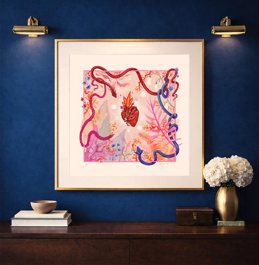 A framed "Heart Aflame" art print displayed on a navy blue wall above a wooden console, illuminated by warm gallery lighting in a modern interior setting.
