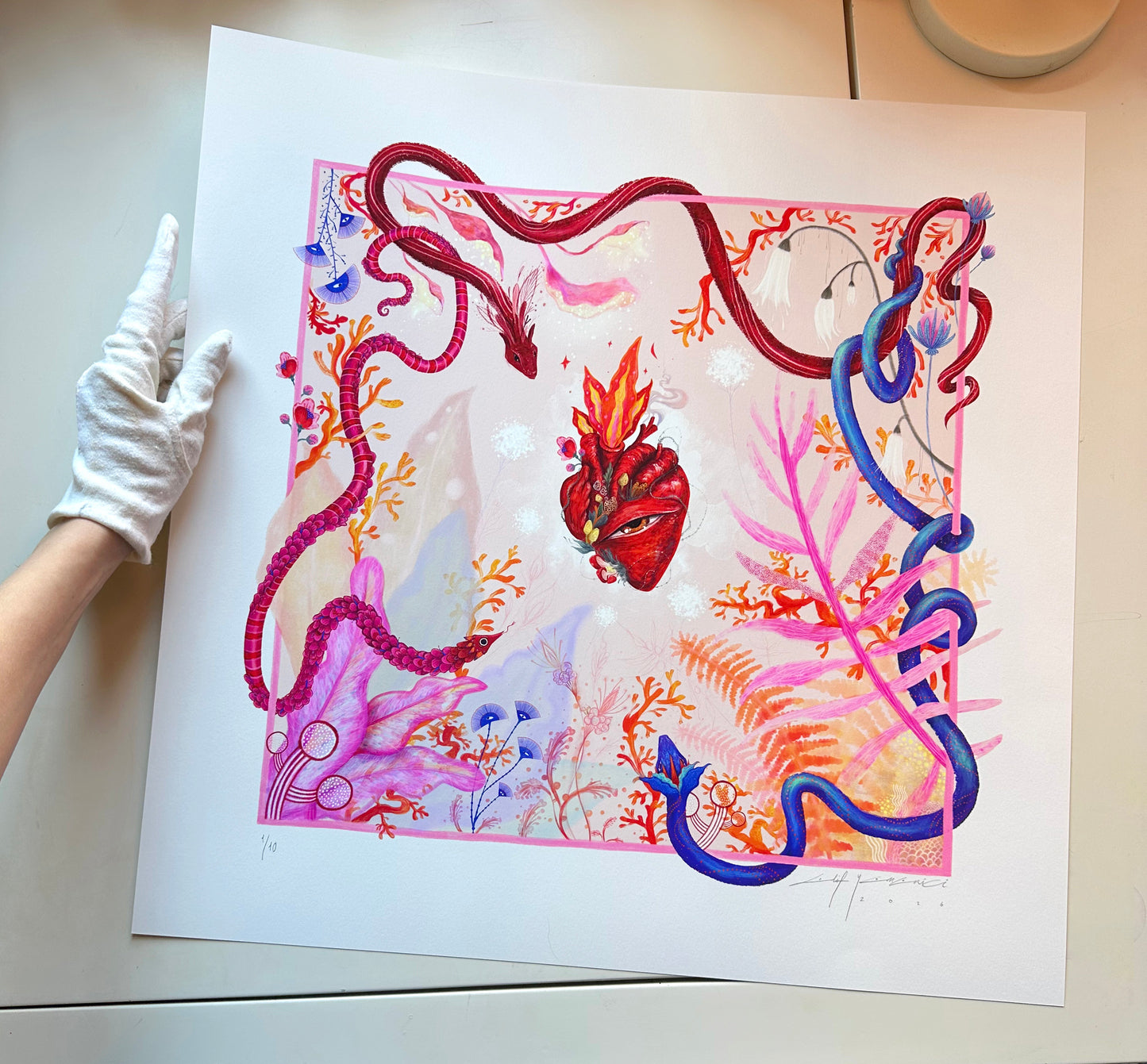 A high-quality art print titled "Heart Aflame" by Elif, featuring a surreal anatomical heart with a central eye and flames, surrounded by vibrant pink and blue serpents and botanical elements.