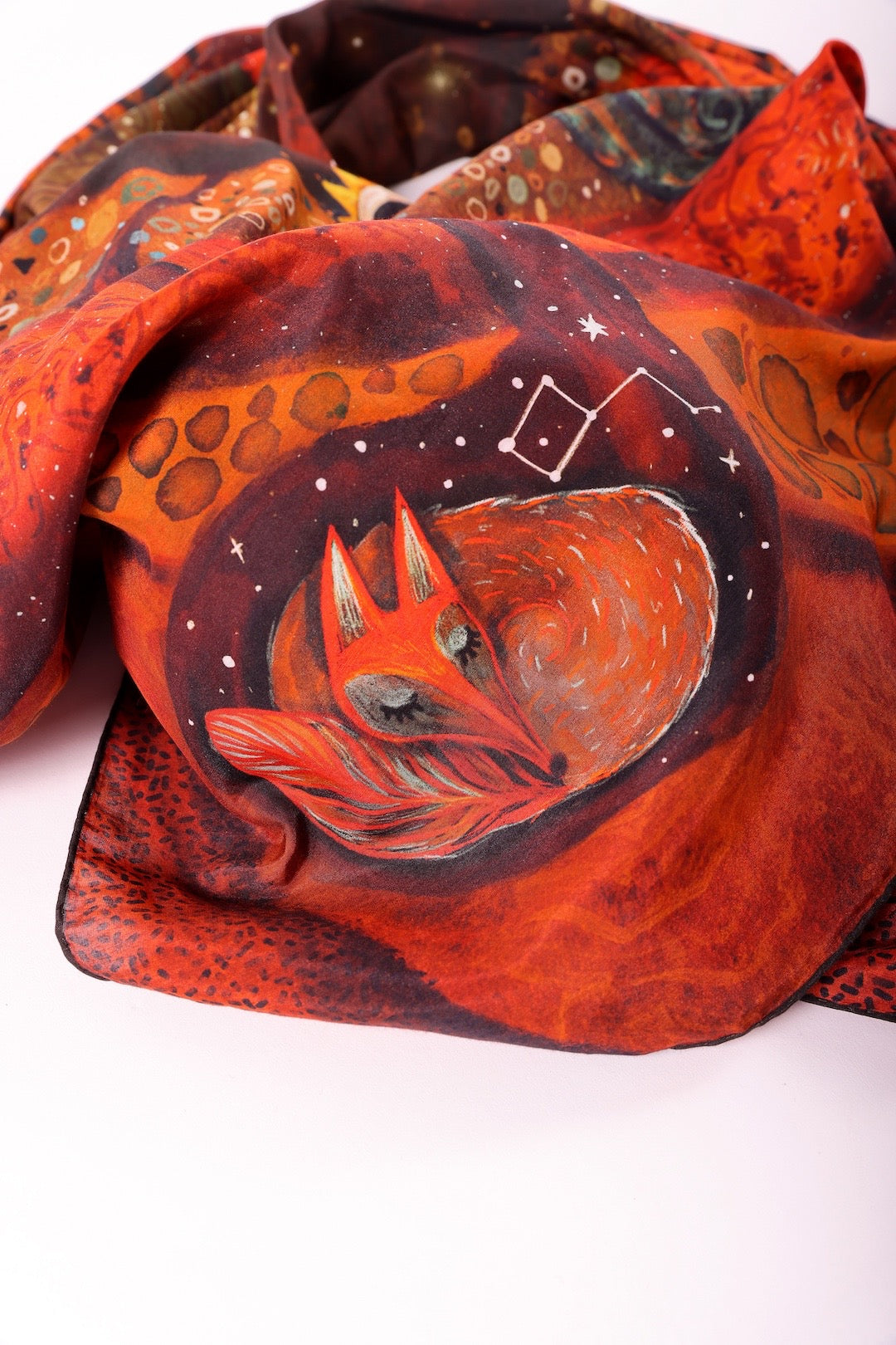 Macro close-up detail of a sleeping fox illustration and cosmic constellations on the surface of a luxury silk-cotton scarf.