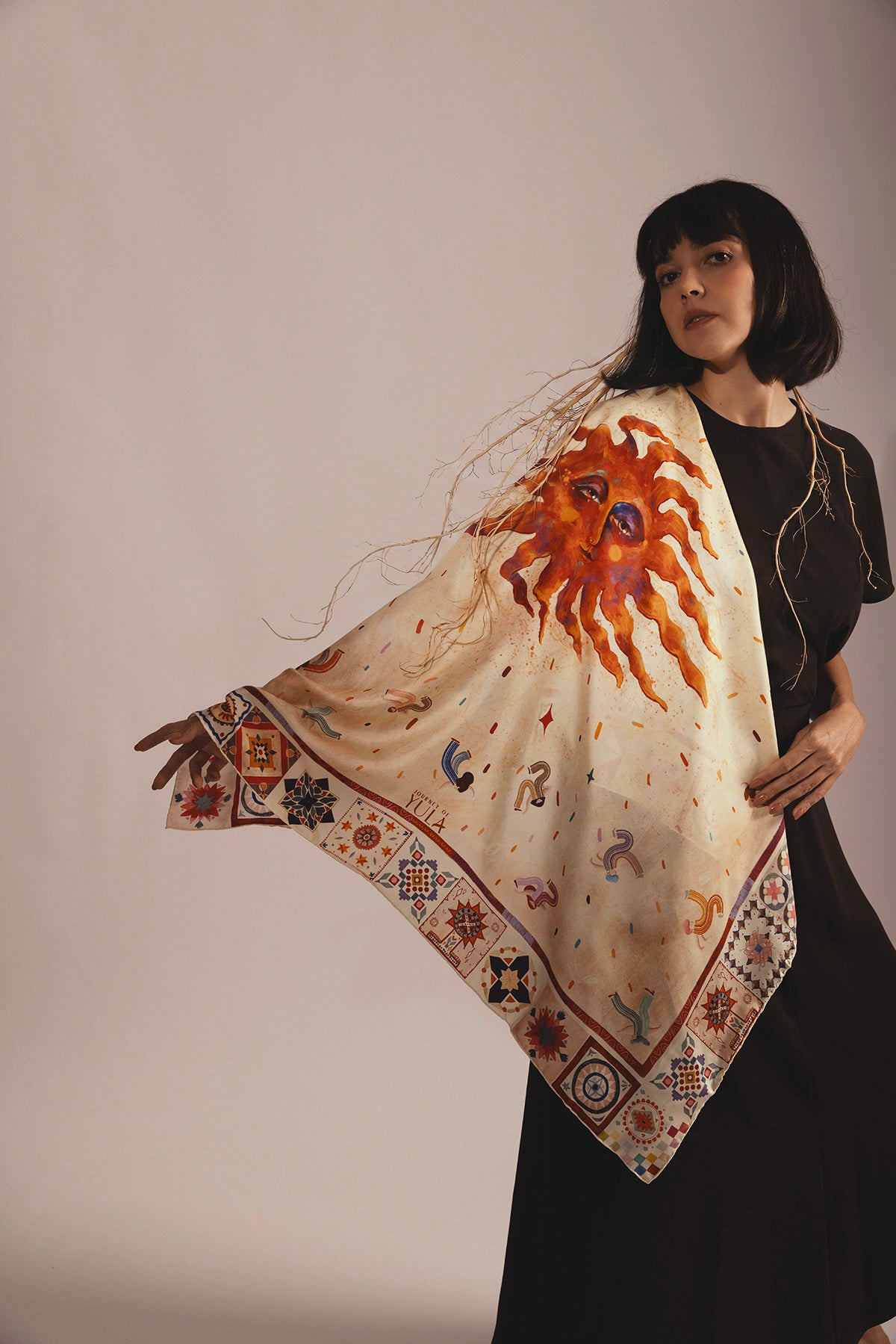 Luxury silk scarf with a vibrant hand-illustrated sun design draped over a woman's shoulder.